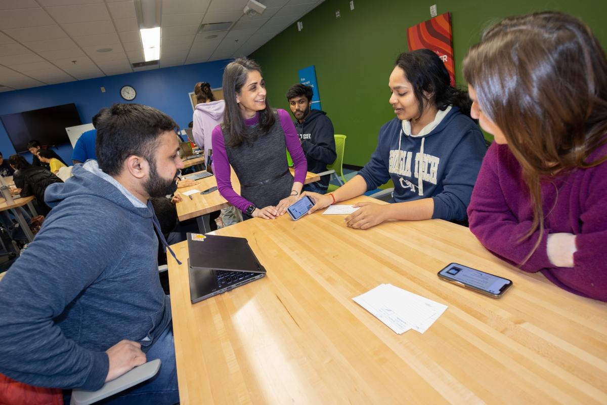 Pamela Bhatti in the classroom working with three students at a table