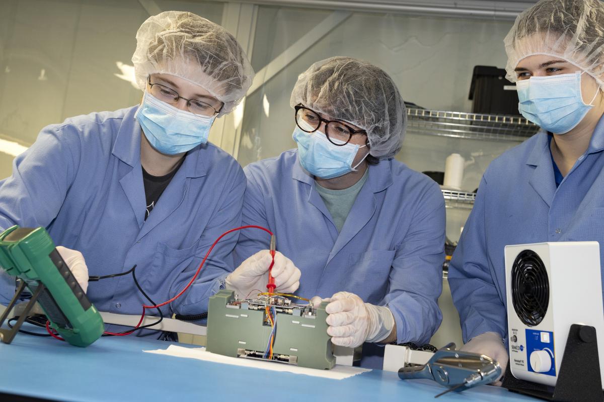 three students in lab gear test the components of a propulsion system