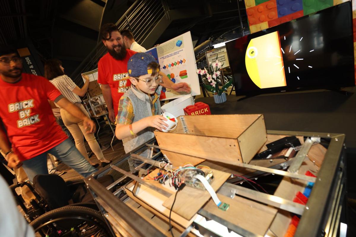 students and a child demonstrate a device that sorts Lego bricks 