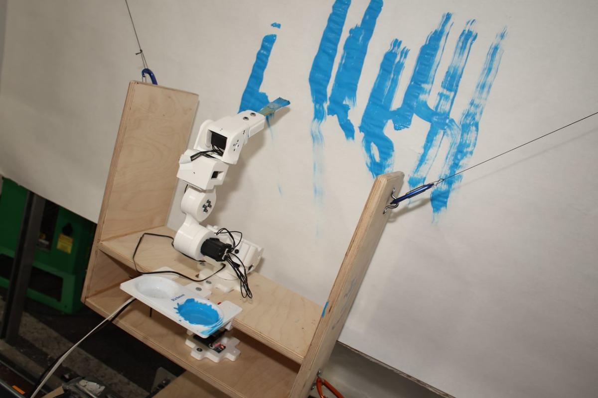 A robotic arm paints on a canvas