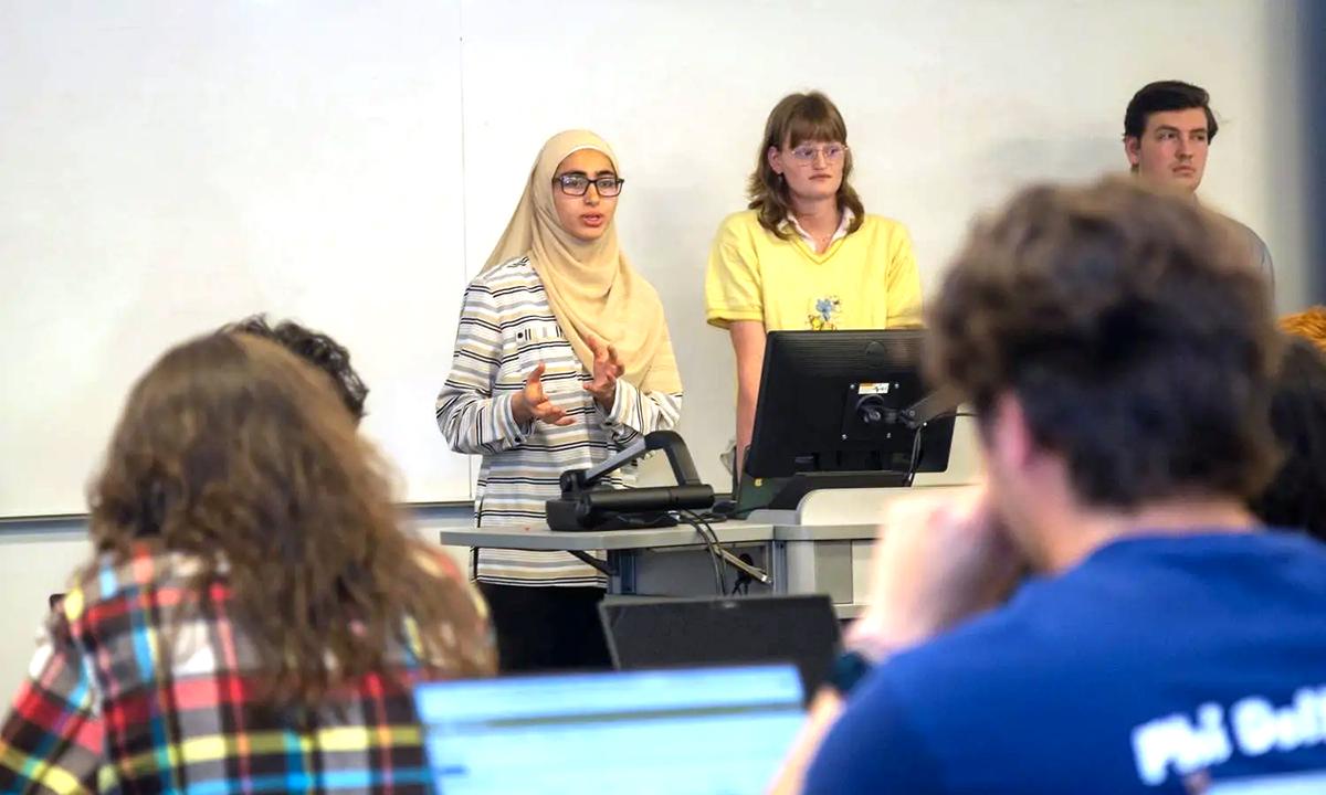 Three students stand while giving a presentation in a classroom.