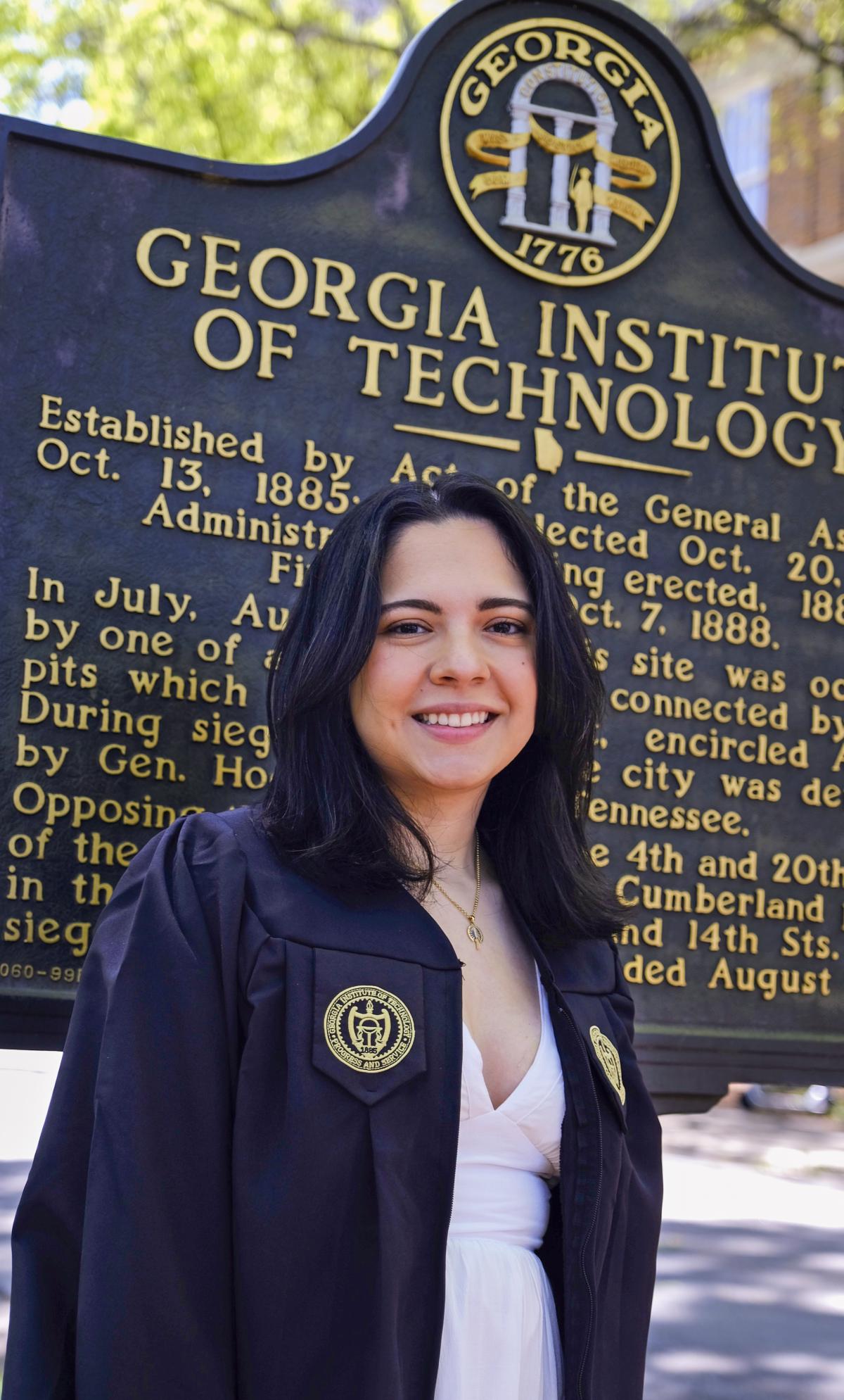 Natalia Barrera Villamizar stands by the Georgia Tech historical marker in her commencement regalia