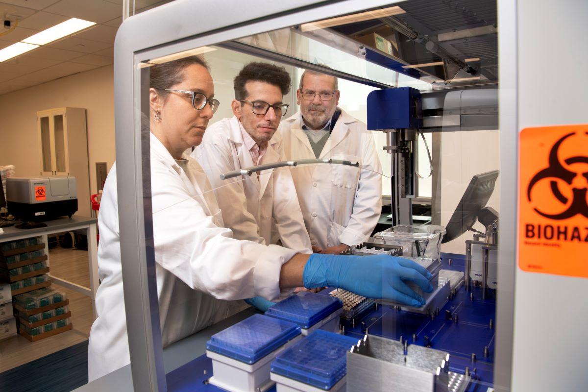 Emory researchers Lorena Chaves, Jose Assumpcao, and Philip Santangelo working at a hood in their lab. (Photo: Jack Kearse)