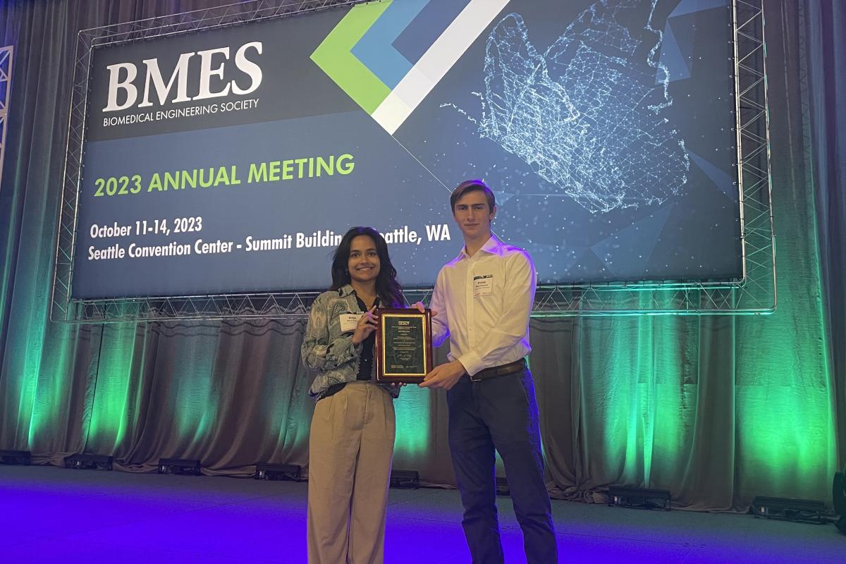 FADpad team members Rhea Prem and Ethan Damiani with their NIH DEBUT award plaque in front of a screen saying BMES 2023 Annual Meeting.