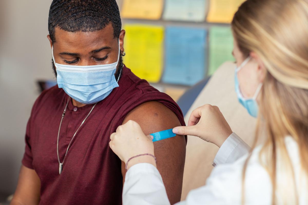 Female nurse puts bandage on arm of male patient after vaccination 