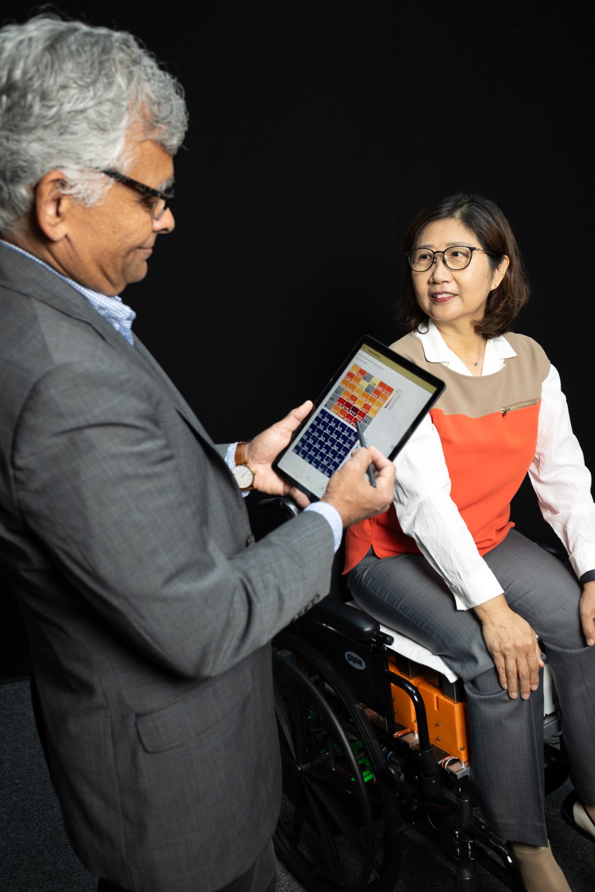Sundaresan Jayaraman looks at a tablet with data while Sungmee Park is seated in the novel wheelchair system