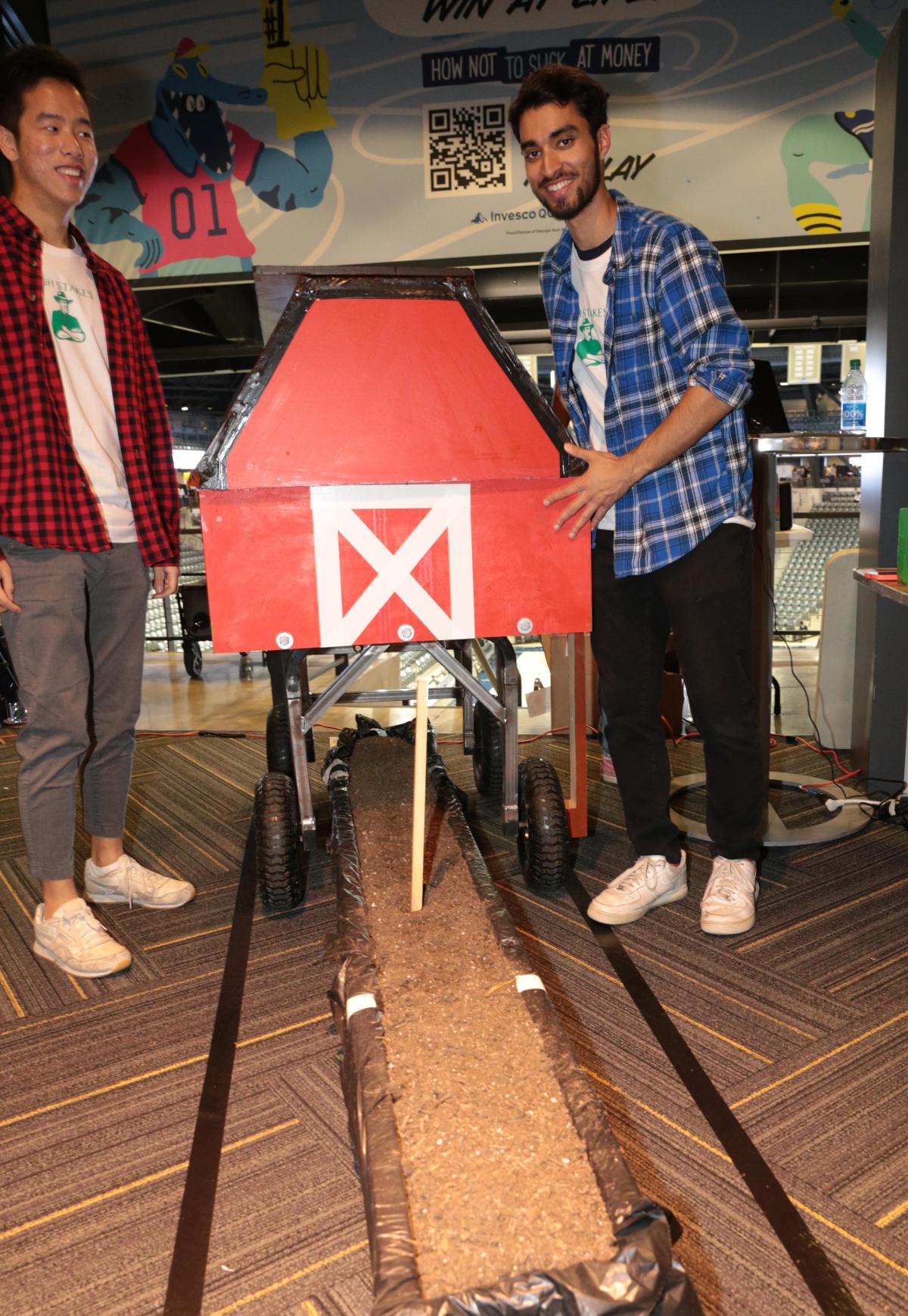 two students with small wooden barn, which put a stick in dirt