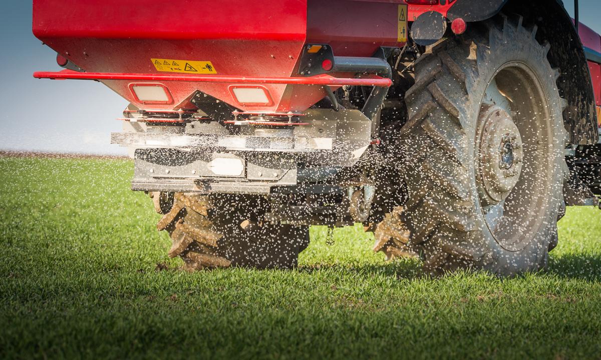 Closeup view of a red tractor spreading fertilizer pellets in a field.