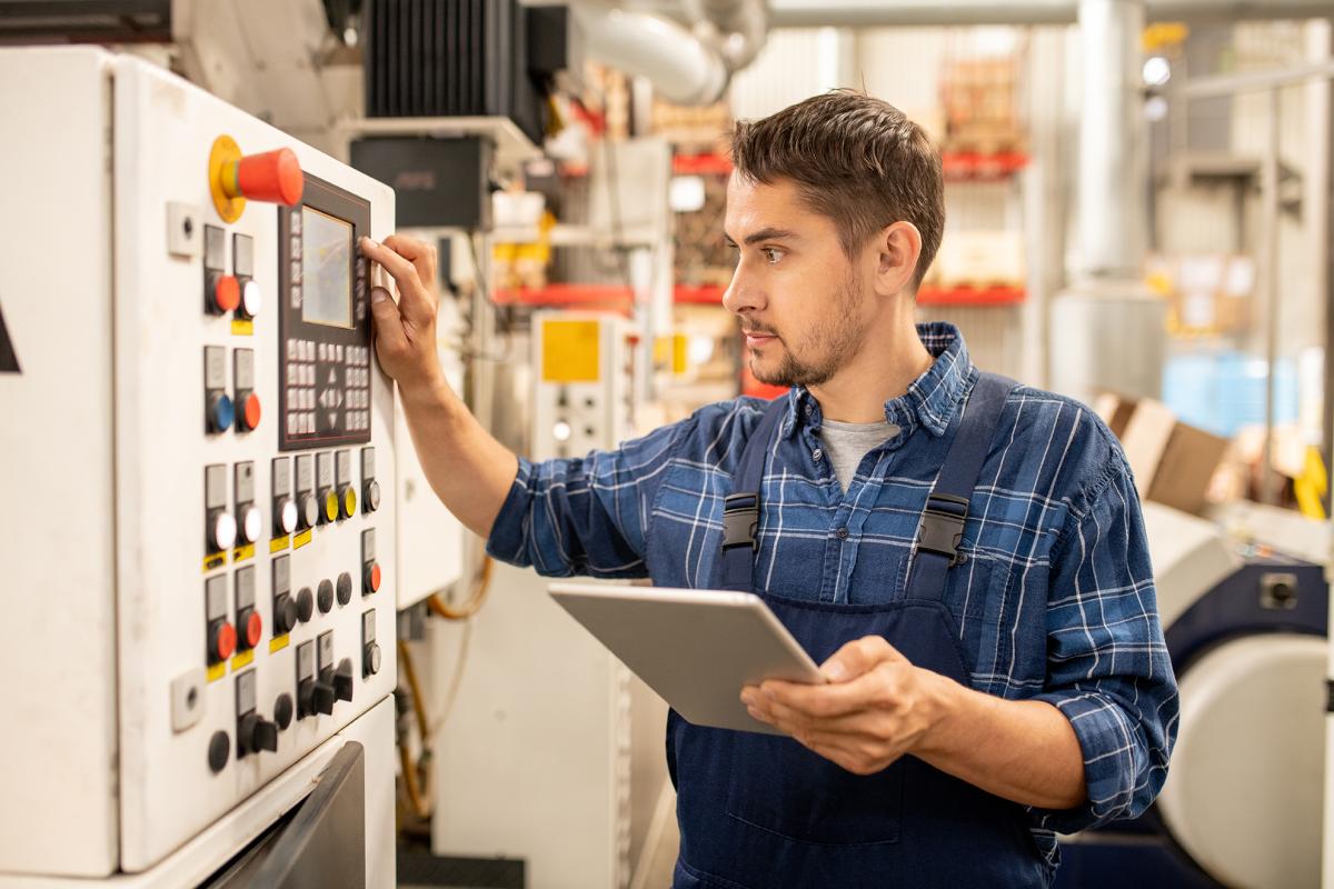 An engineer checks data on a tablet computer and an industrial control panel.