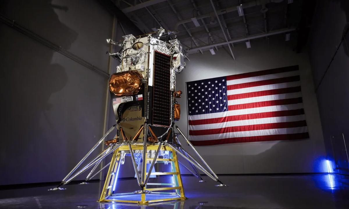 The six-legged Odysseus lunar lander after assembly was completed with a spotlighted U.S. flag on the wall behind it. (Photo Courtesy: Intuitive Machines)