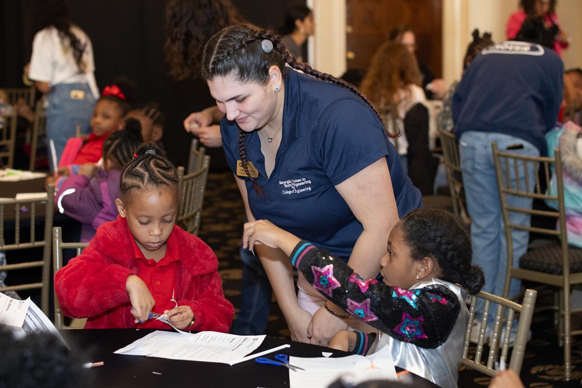 A Georgia Tech student helps two young girls with the design and construction of paper rockets. (Photo: Veronica Soroka)