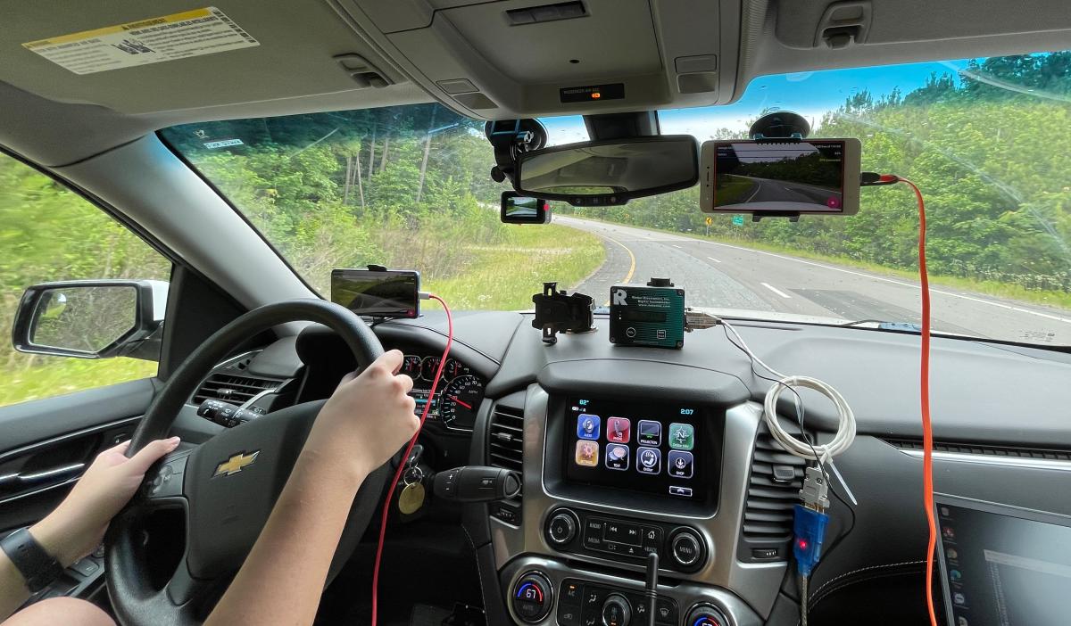 a vehicle dashboard with a smartphone mounted to the windshield as the vehicle approaches a curve in the road ahead