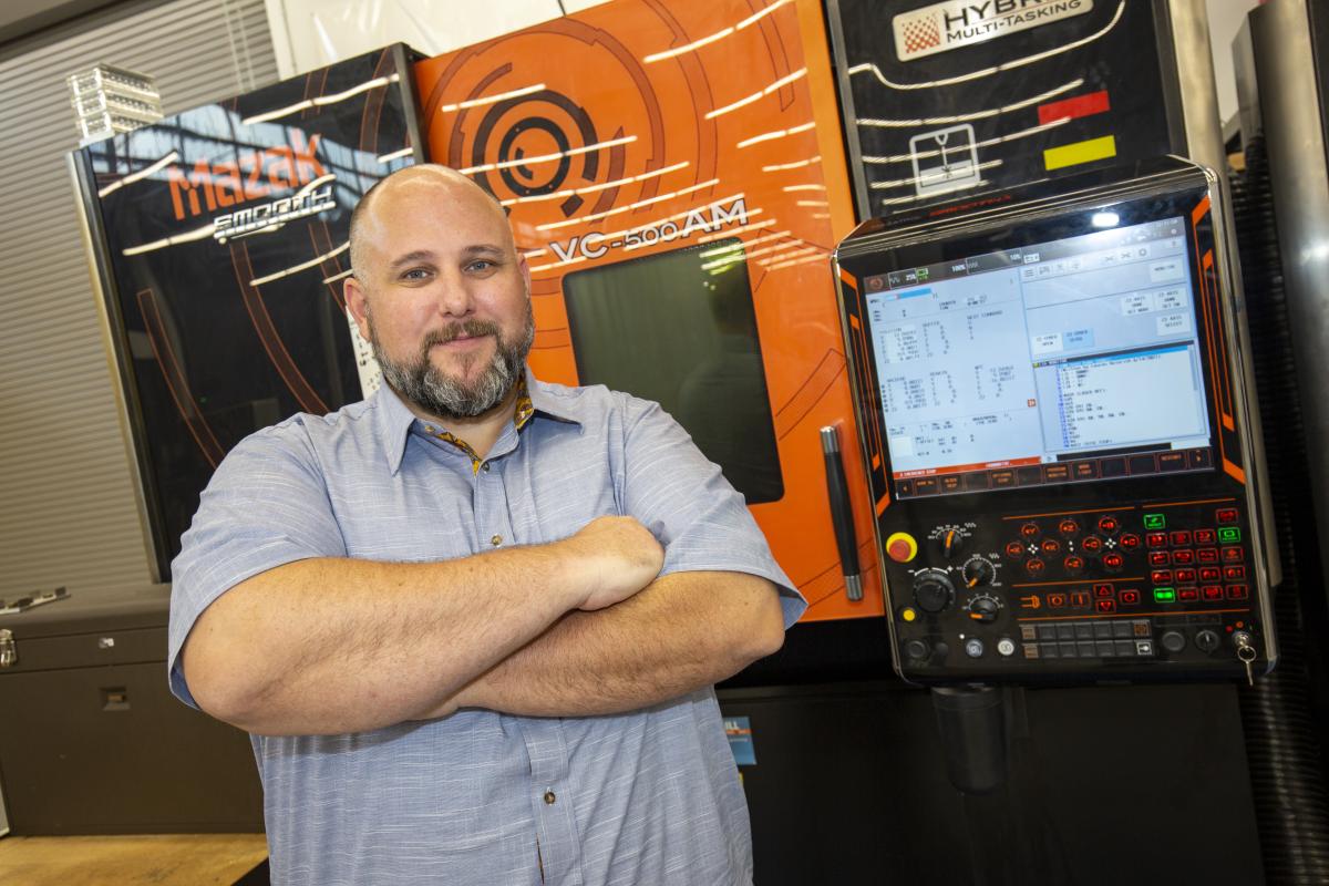 Aaron Stebner stands in front of a piece of machinery in the Advanced Manufacturing Pilot Facility