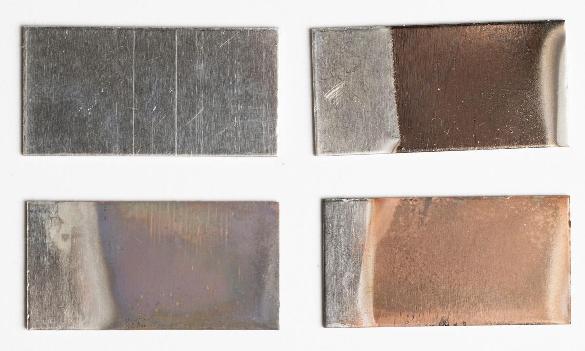 Four rectangular pieces of stainless steel. Top left, an unmodified sample. Bottom left, a discolored piece after the electrochemical etching process. Top right, a slightly orange piece after four minutes of copper ion deposition. Bottom right, a more orange sample after 15 minutes of copper ion deposition. (Photo: Candler Hobbs)