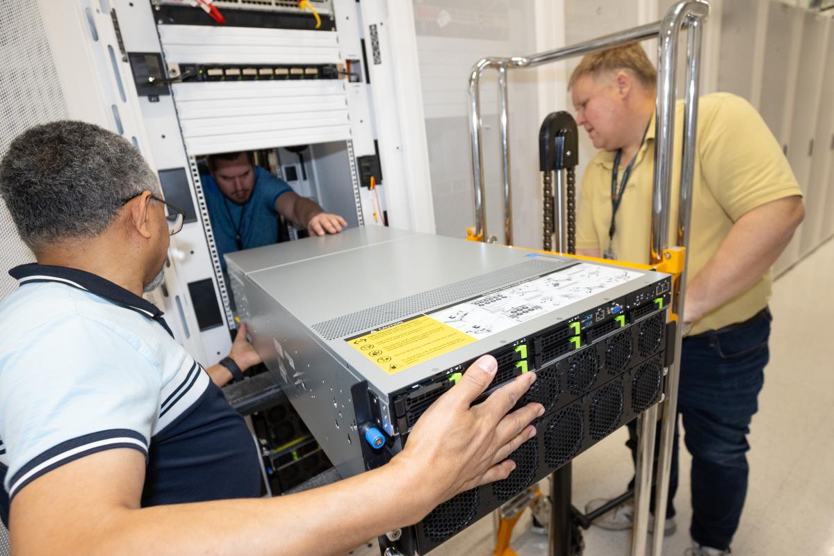 Three men load computing equipment into a cabinet