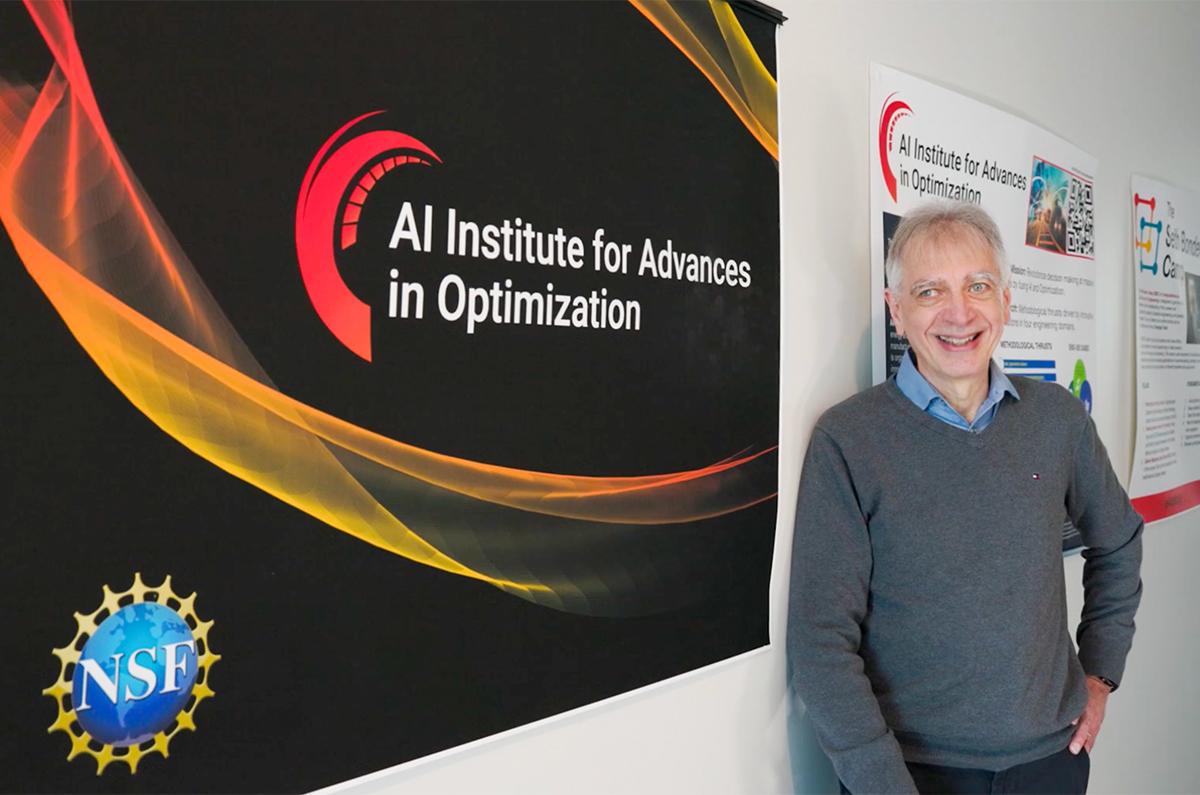 Pascal Van Hentenryck in front of an "AI Institute for Advances in Optimization" poster