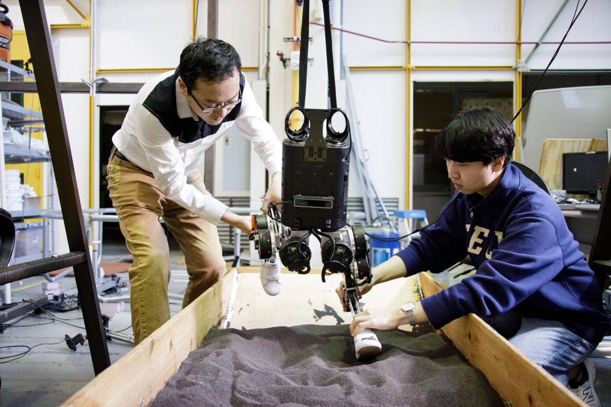 ME Assistant Professor Ye Zhao and a student work in the lab with a bipedal robot in a sandbox
