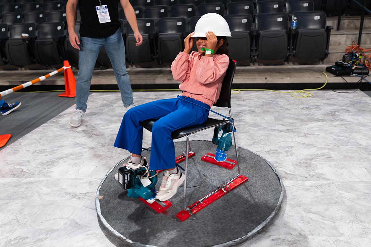 A student in a hardhat rides on a glider device at STEM fest