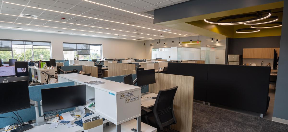 Open workspace with cubicles and computer monitors as well as a break and kitchen area.