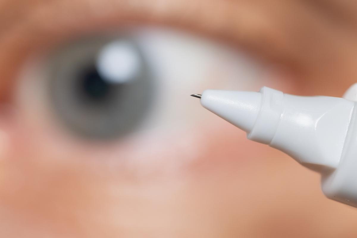 A 1 mm hollow microneedle at the tip of a white injection device with an eye out of focus in the background.