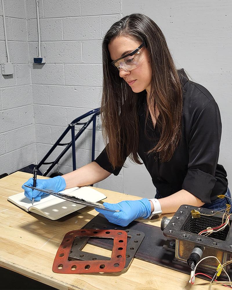 Amanda Nummy takes notes at a lab bench with car battery enclosure materials