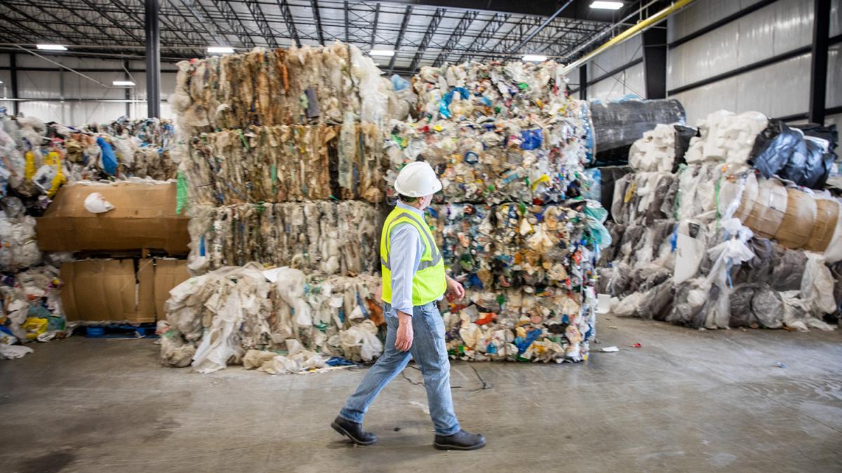 a man walks in front of many bales of plastic in a warehouse