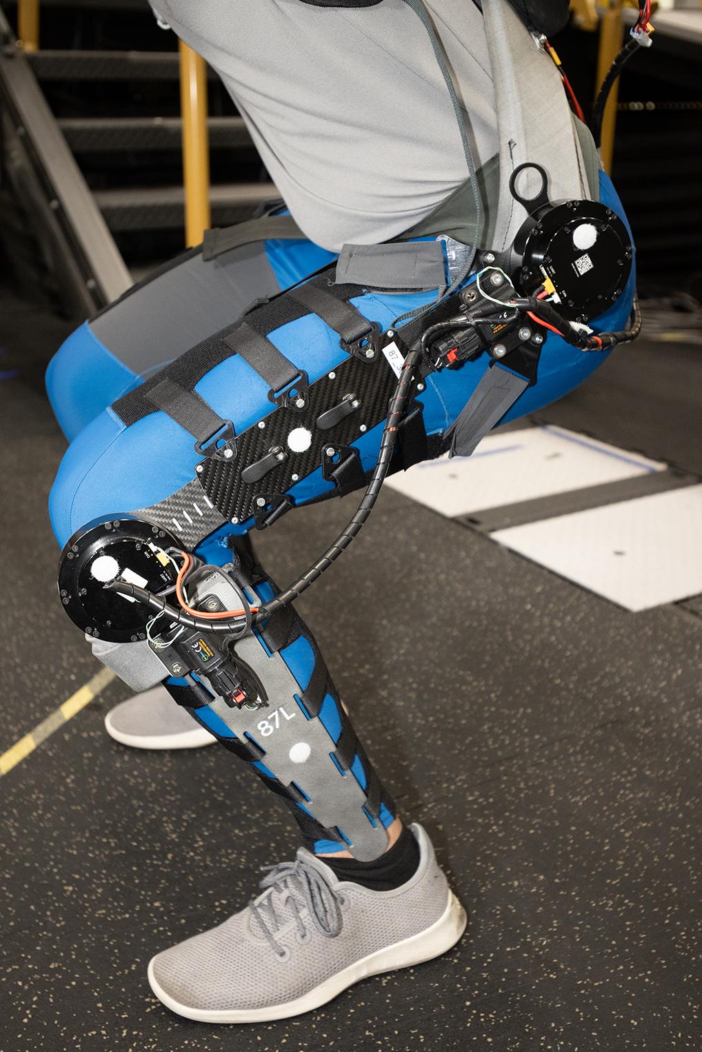 A person from the waist down partially squatting while wearing a robotic exoskeleton on their legs.