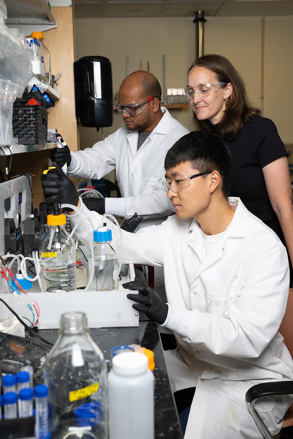 Three people work with equipment at a lab bench