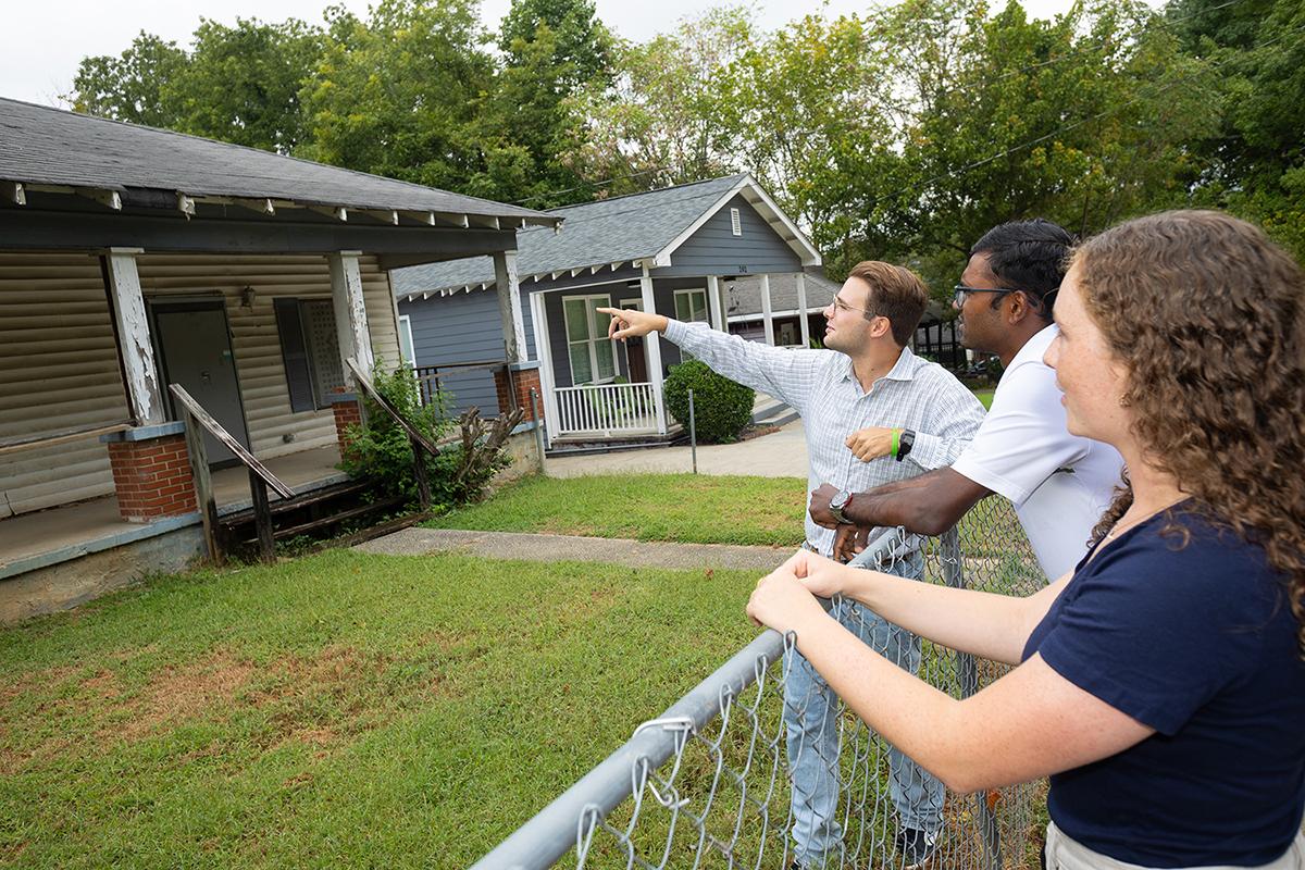 Three students point and look at a house from the front yard