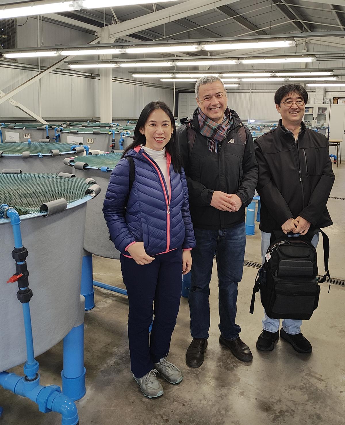 Three people stand in a warehouse with aquaculture facilities