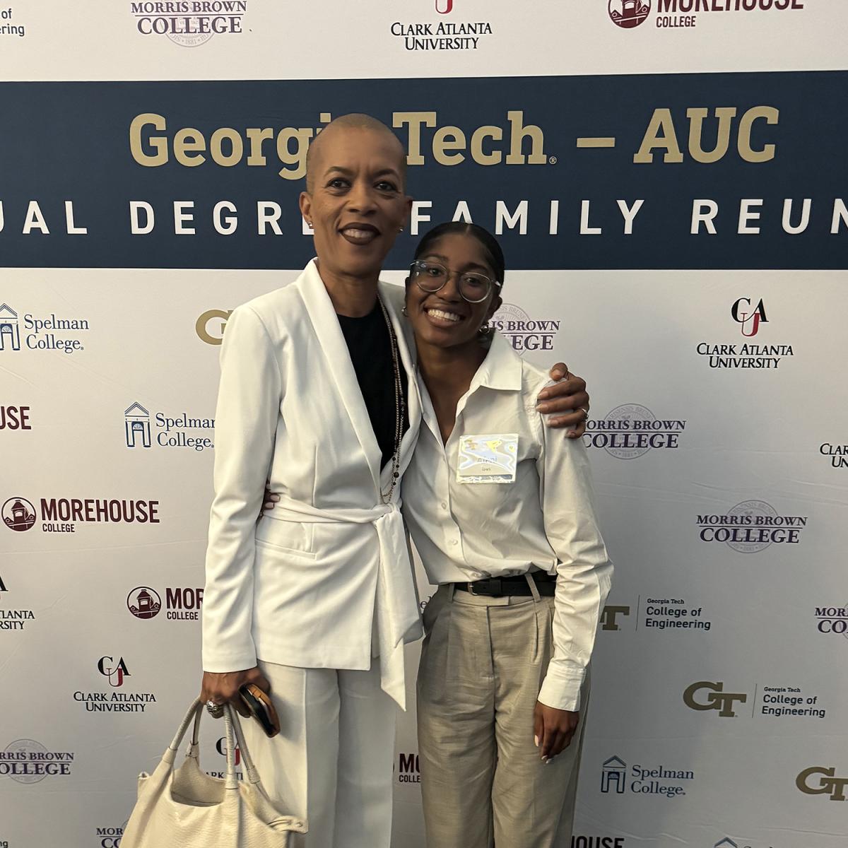 Two women pose in front of a background with university logos and text "Georgia Tech - AUC Dual Degree Family Reunion"