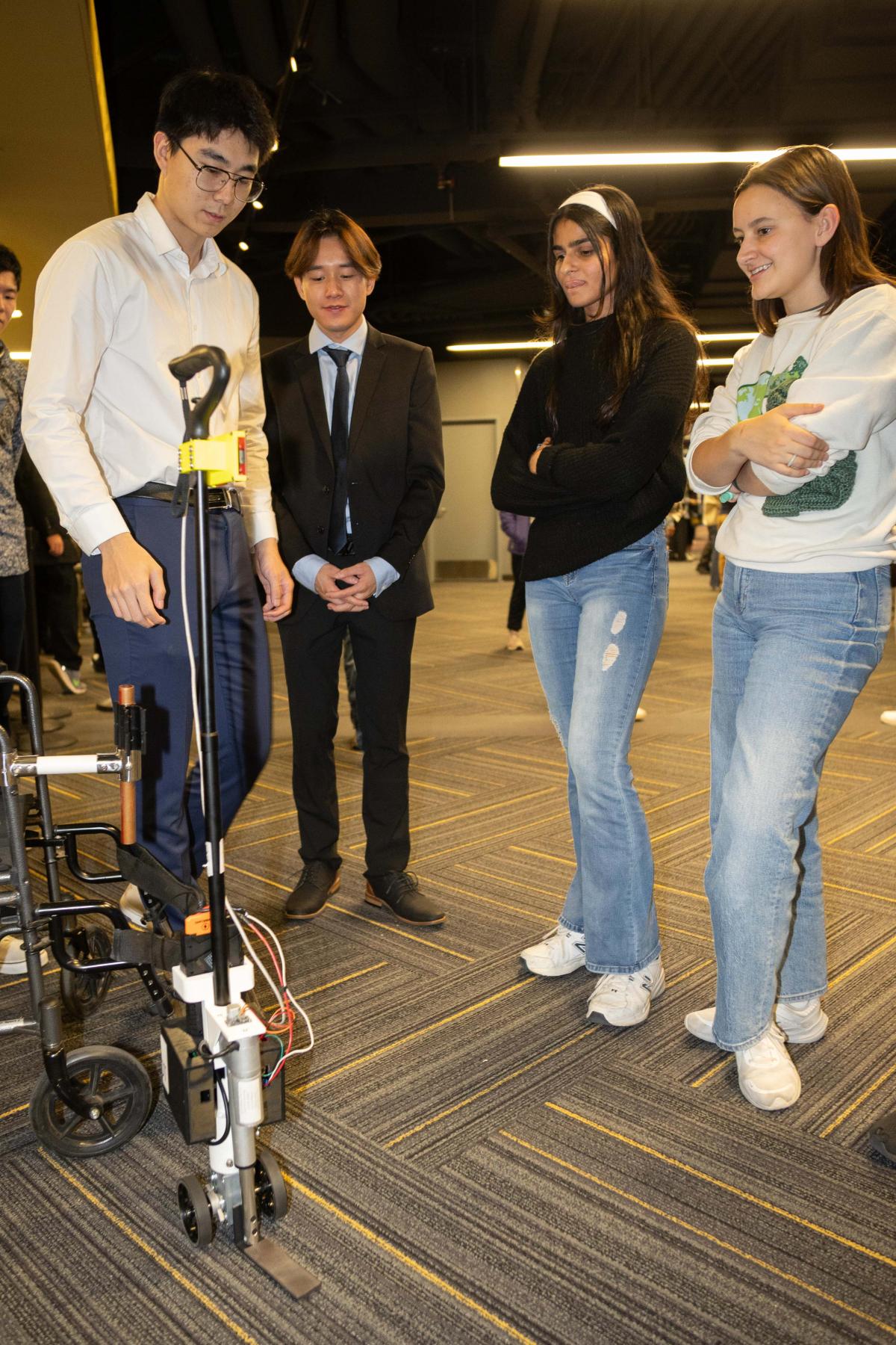 four students look at a walking-device machine that helps open doors