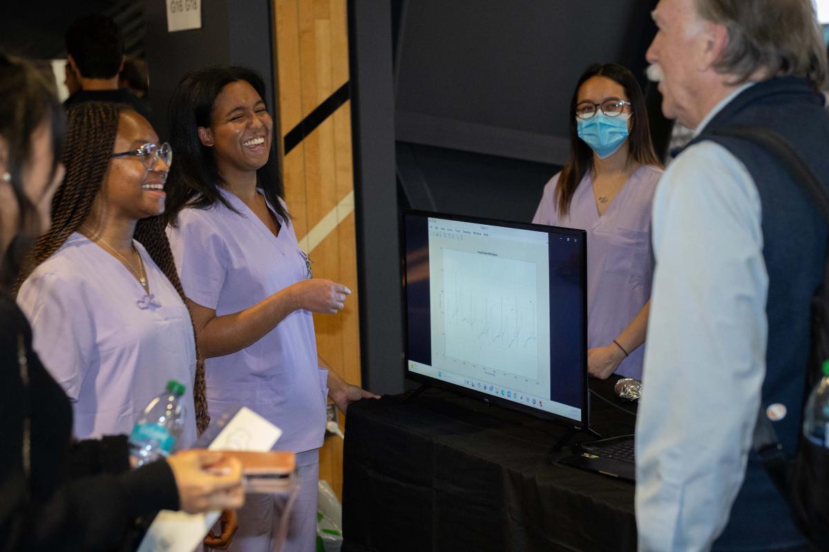 three female students in purple scrubs talk to a male judge