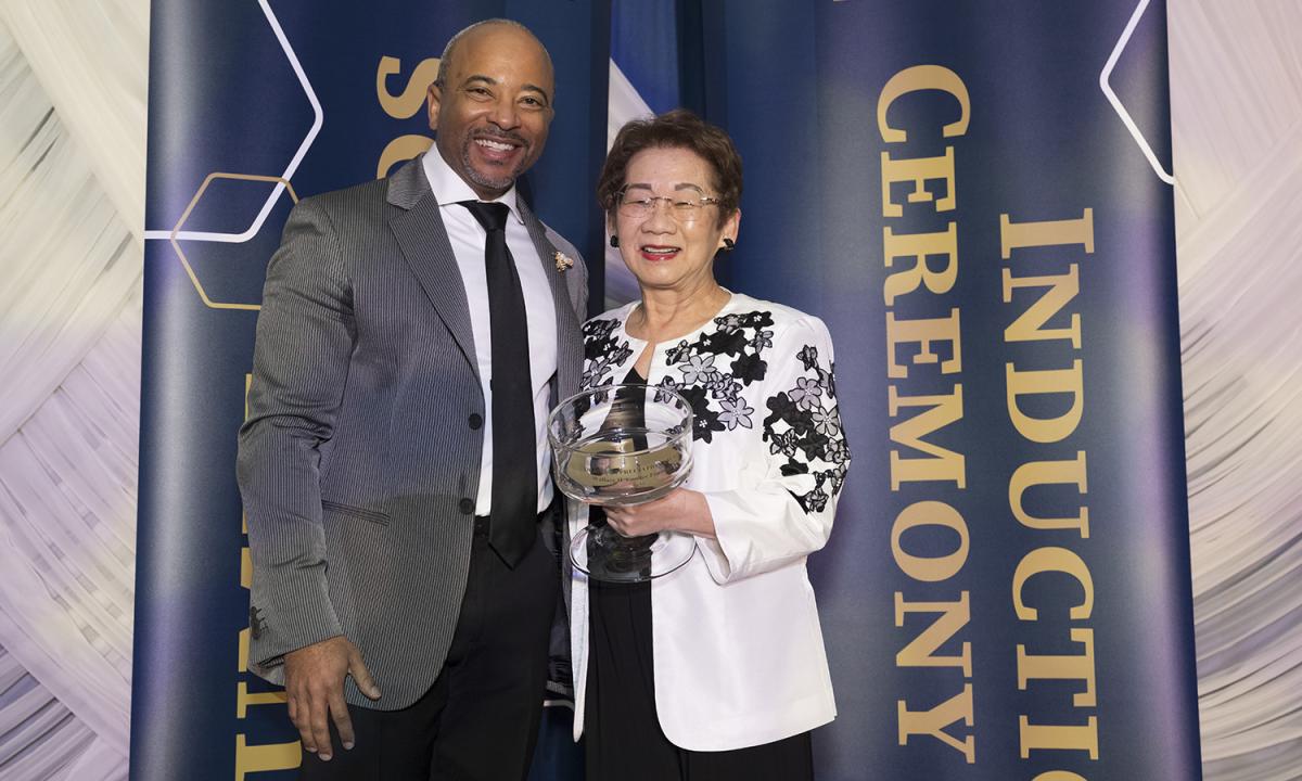 Dean Raheem Beyah and Sue Van, holding an award, stand in front of decorative banners