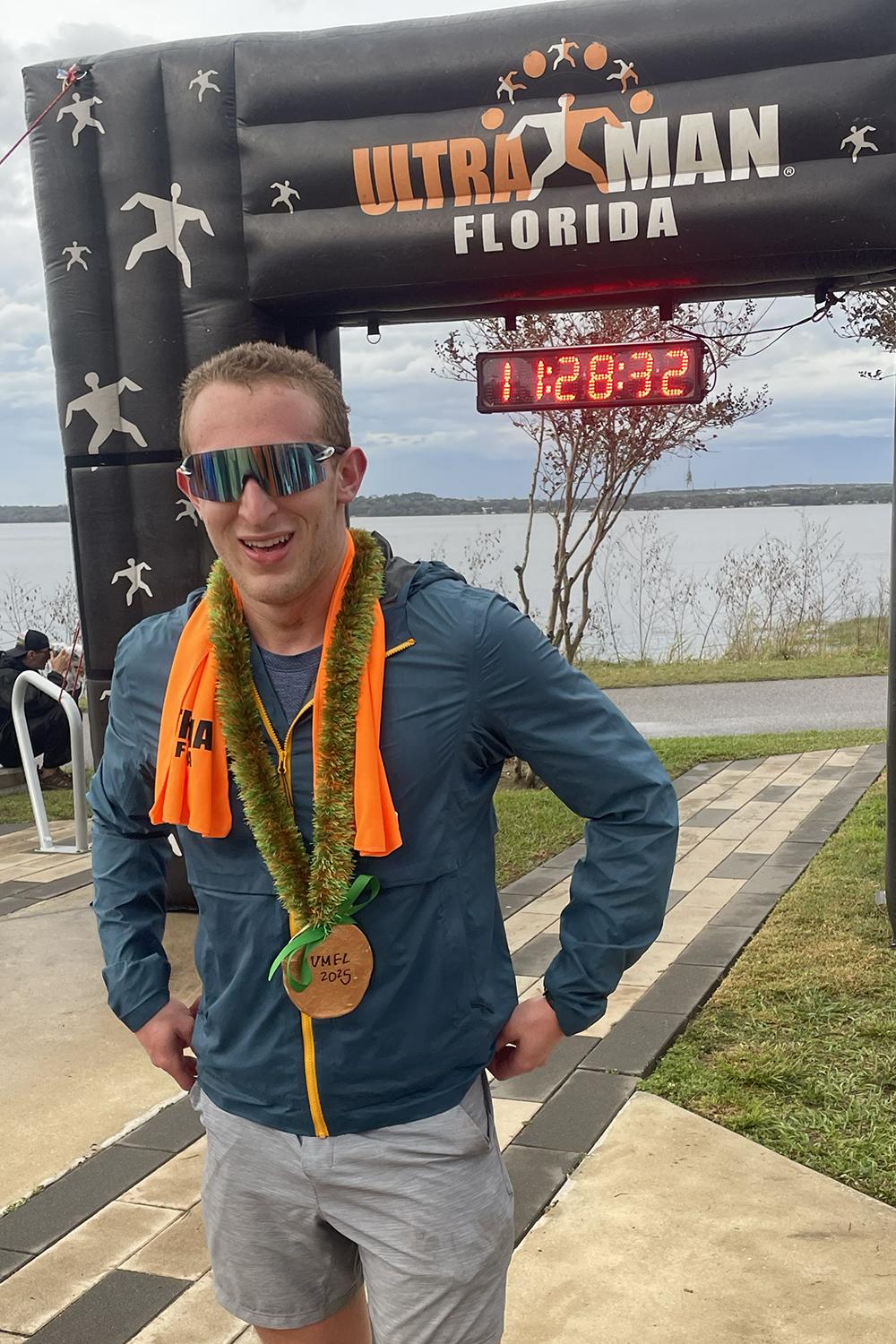 Jacob Beldick wearing his medal and standing in front of the finish line for the Ultraman Florida race.