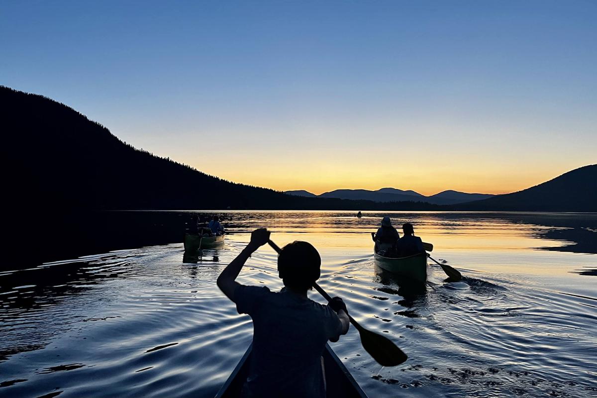 Silhouette view of three canoes at sunset on a lake. James Shin is paddling closest to the viewer.