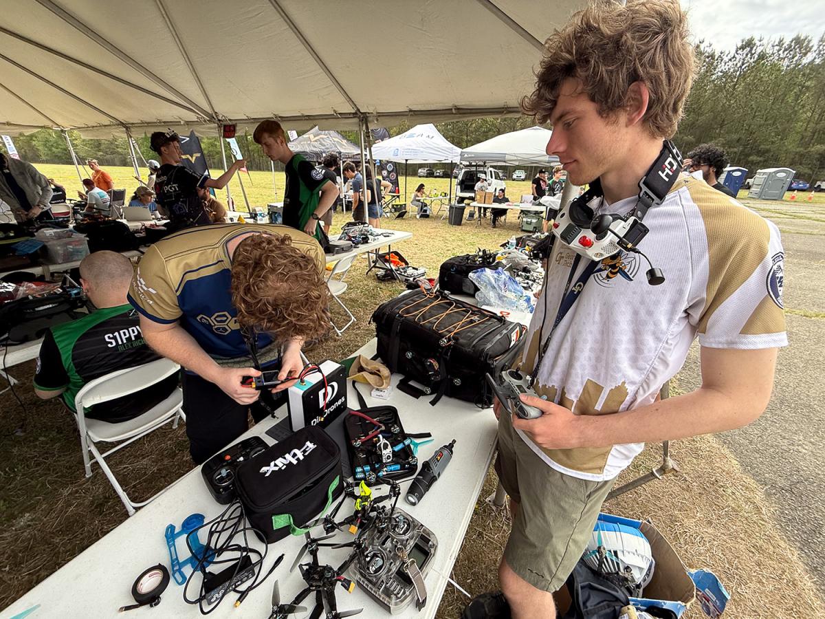 Two people make adjustments to a drone outside