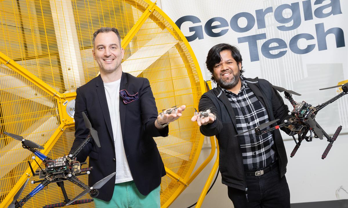 Two people hold large and small drones in a flight lab