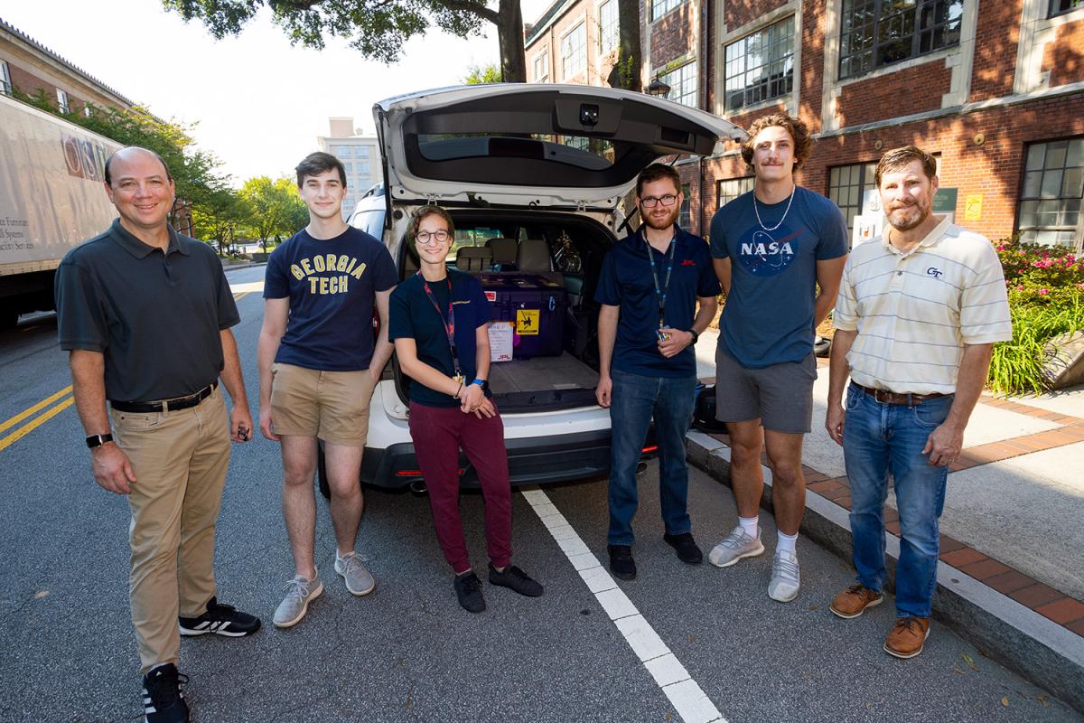 people gather with a vehicle holding a CubeSat for transportation