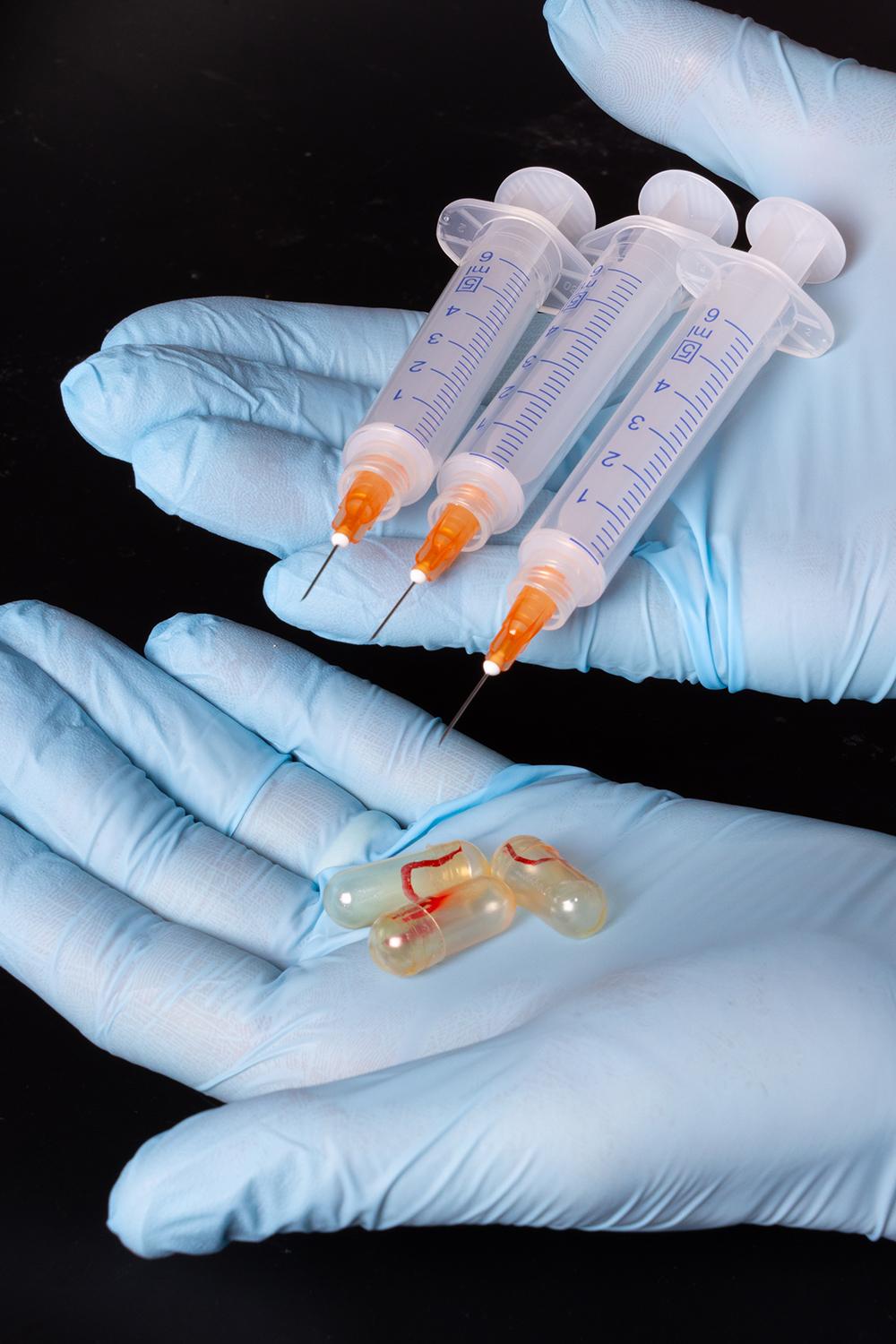 a closeup of gloved hands holding hypodermic needles and specialized capsules