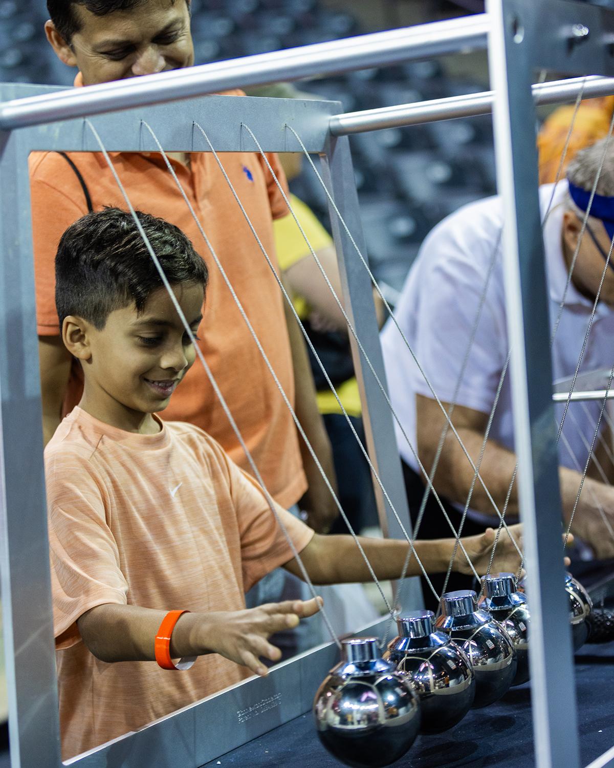 A student swings large suspended balls in a massive Newton's Cradle device.