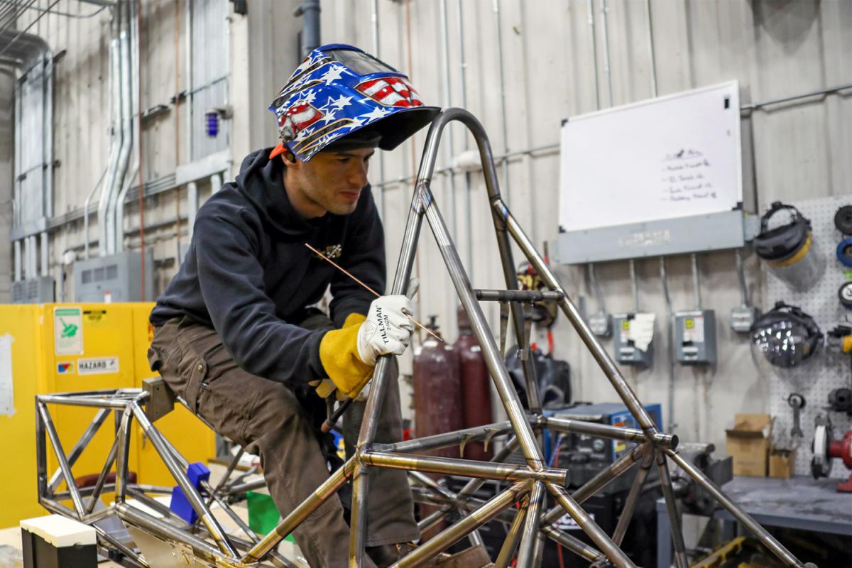 a student works on a vehicle frame in a warehouse