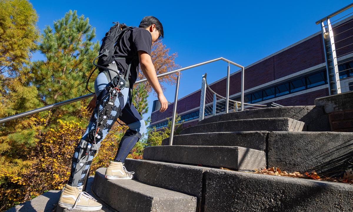 Ph.D. student Ethan Park walks up a set of stairs to demonstrate an AI-powered hip and knee exoskeleton.
