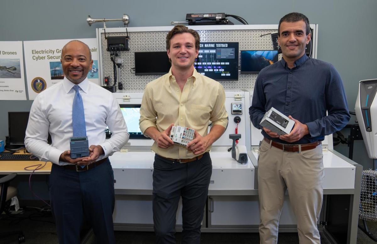 Three people standing in front of an electronics lab bench holding devices.