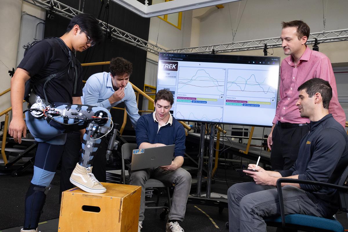 Ethan Park conducts test with a leg exoskeleton while researchers Matthew Gombolay and Aaron Young work with other Ph.D. students on the controller for the device they created using an AI tool that greatly simplifies the process.