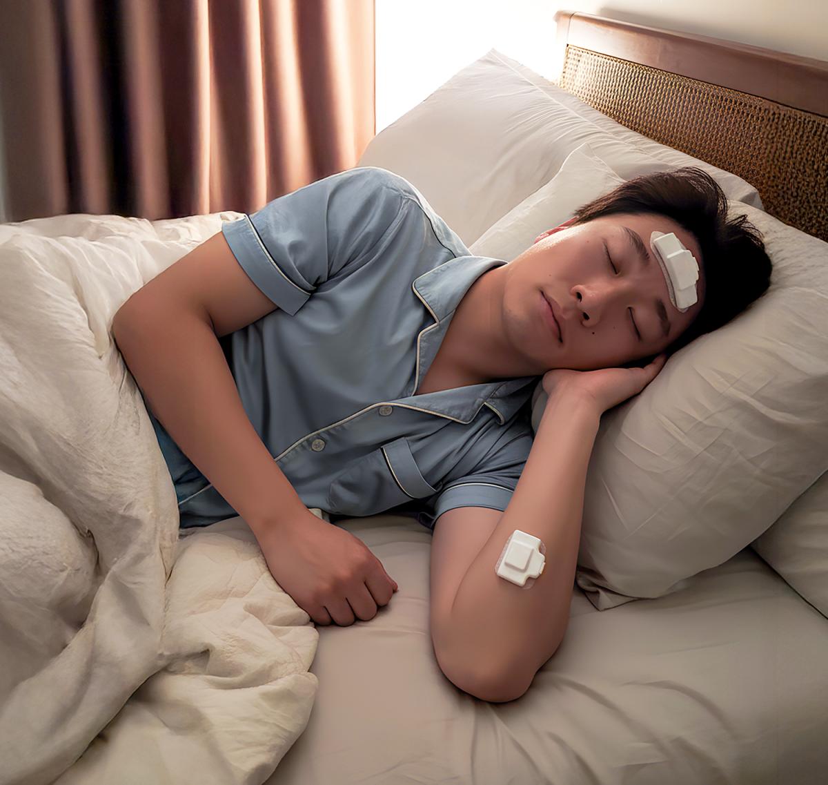 a person sleeping in bed with sensors on his forehead and arm