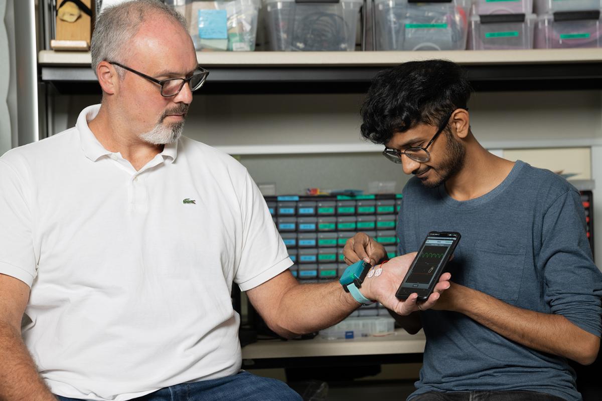 Two people in the lab make adjustments to a wristband device