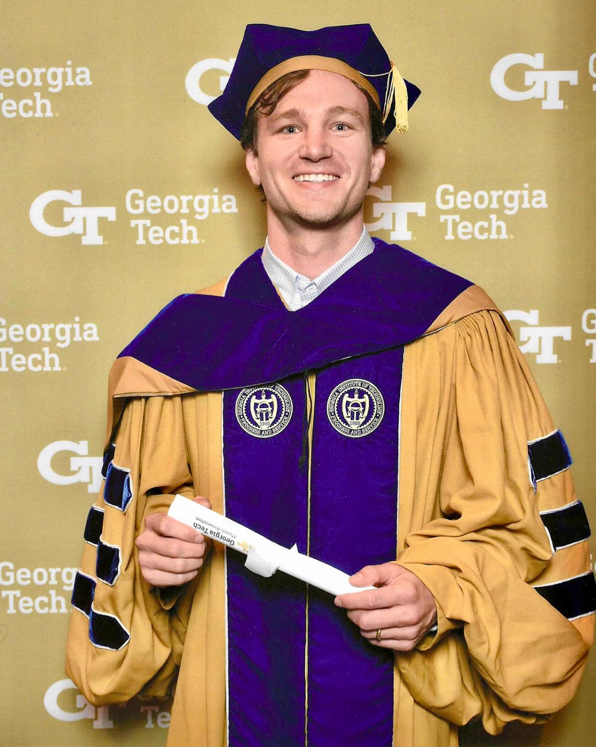 Ryan Pickren in Ph.D. regalia holding a diploma at Commencement