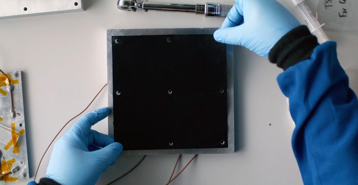 gloved hands apply a carbon cooling pad on an electronic component 