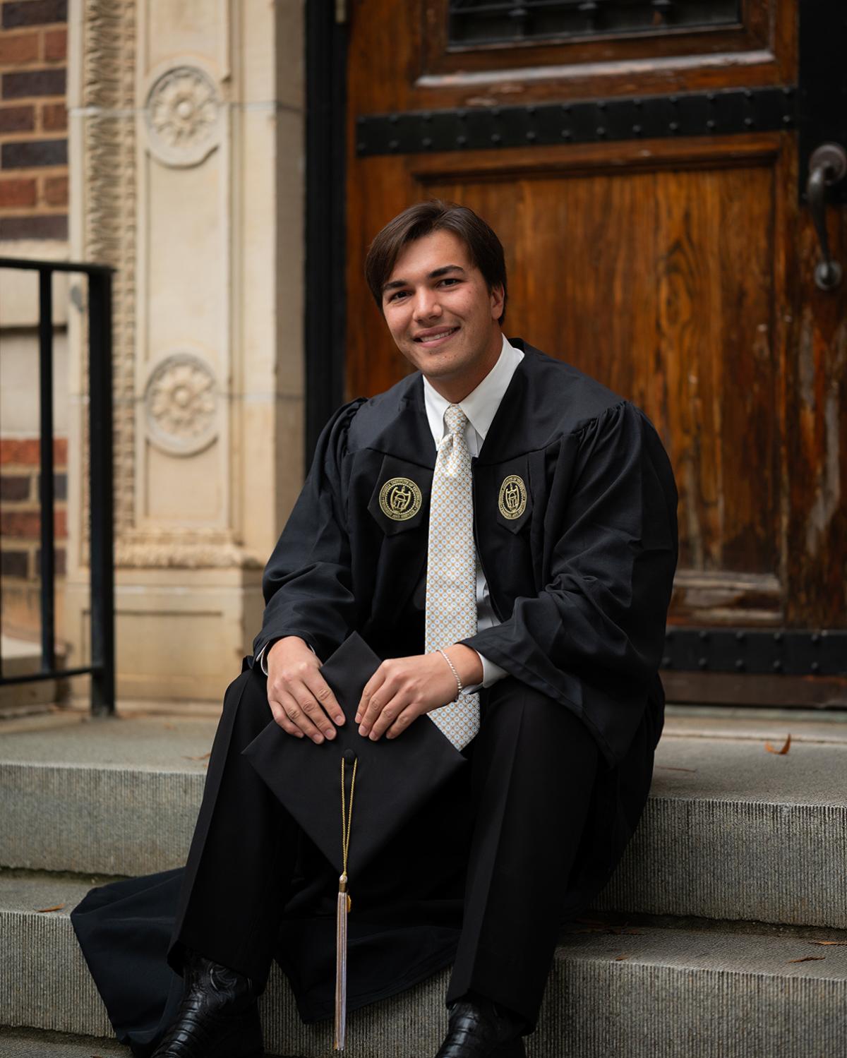 Cole Rogers sits on steps in his graduation regalia.